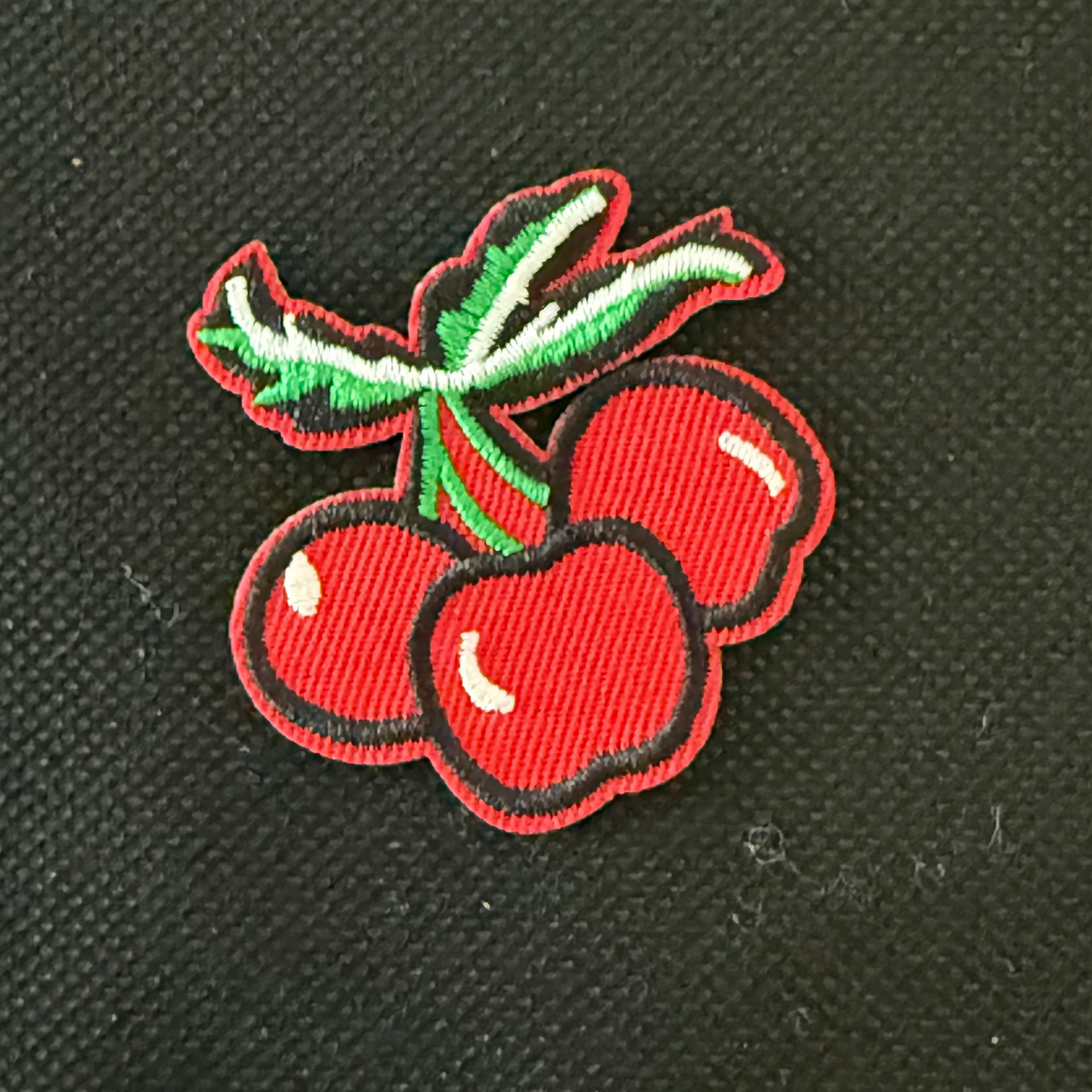 Embroidered patch of cherries on a black background