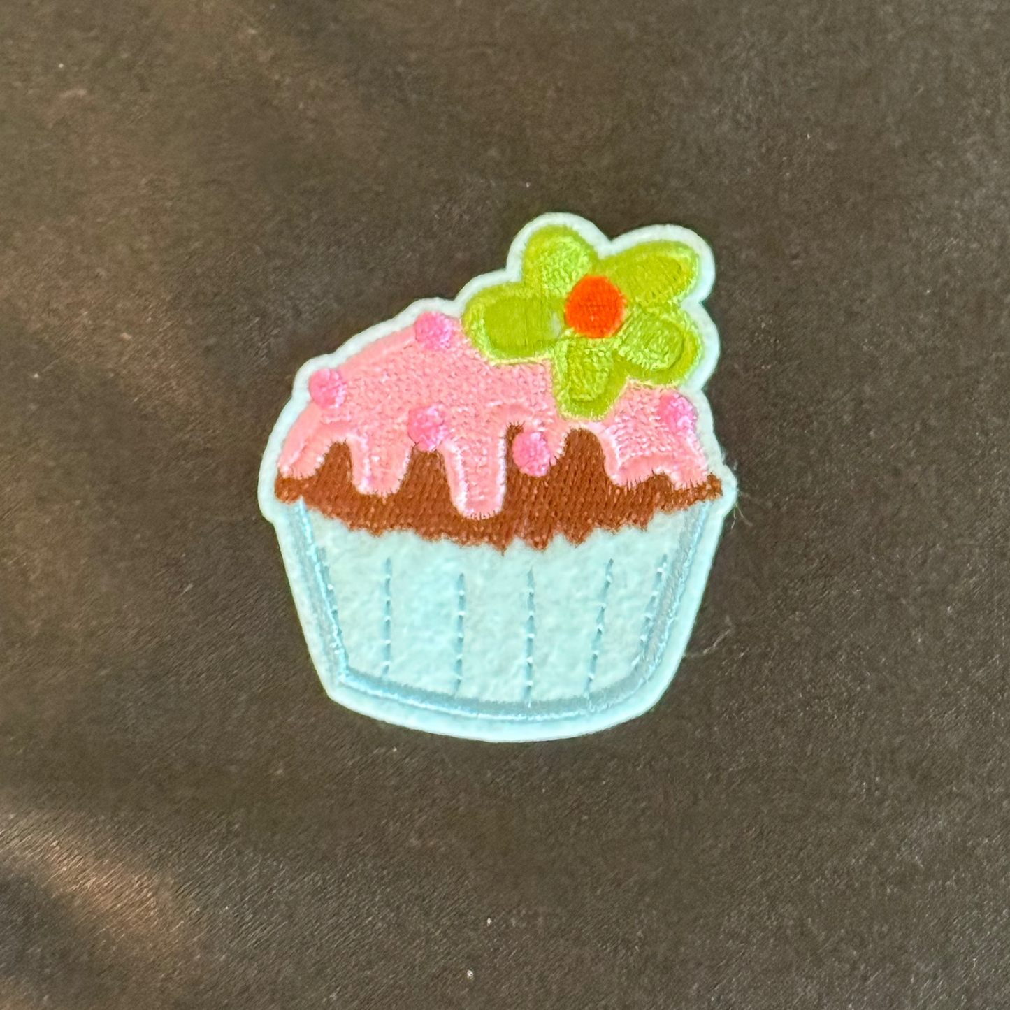 Cupcake-shaped patch with pink icing and green leaves on a black background