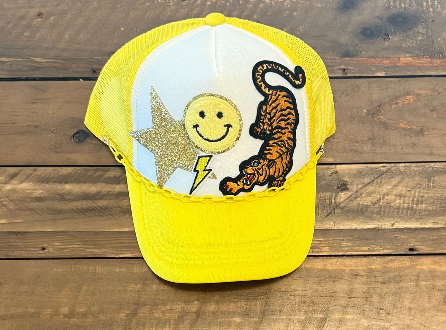 Yellow and white cap with a gold star patch, yellow smiley face patch, yellow lightning bolt patch, and a tiger patch.