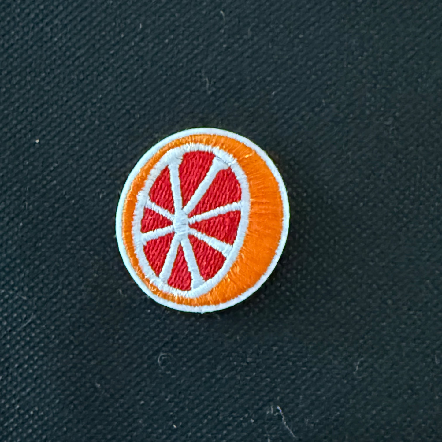 Circular patch with orange and red design on a dark fabric background