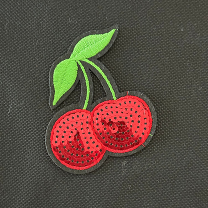 Embroidered patch of two red cherries with a green leaf on a black background