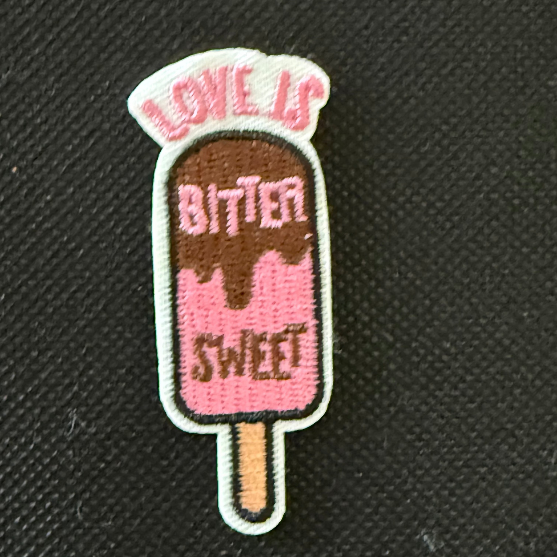 Embroidered patch of a popsicle with text on a black background