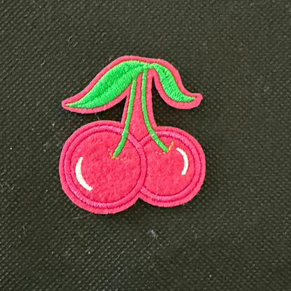 Embroidered pink cherries with green stems on a black background
