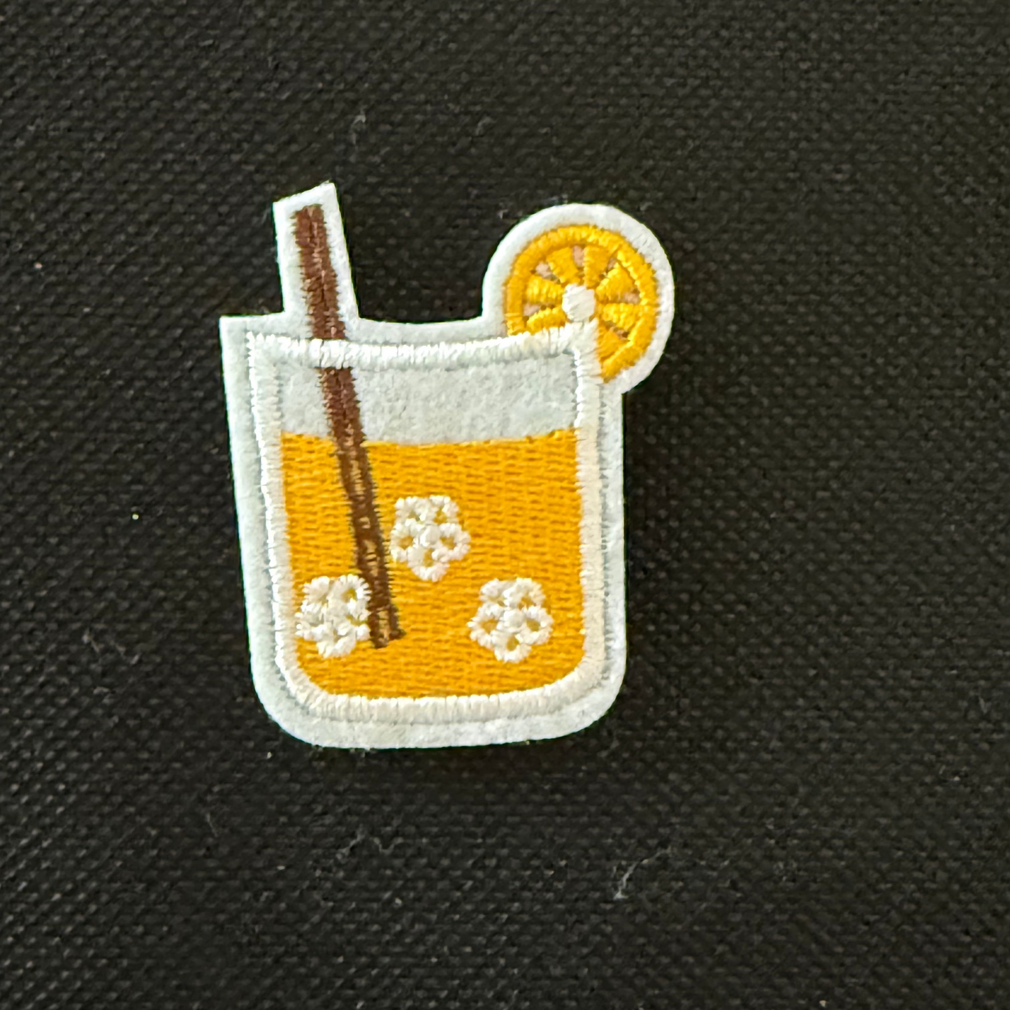 Embroidered patch of a cocktail with an orange slice and straw on a black background