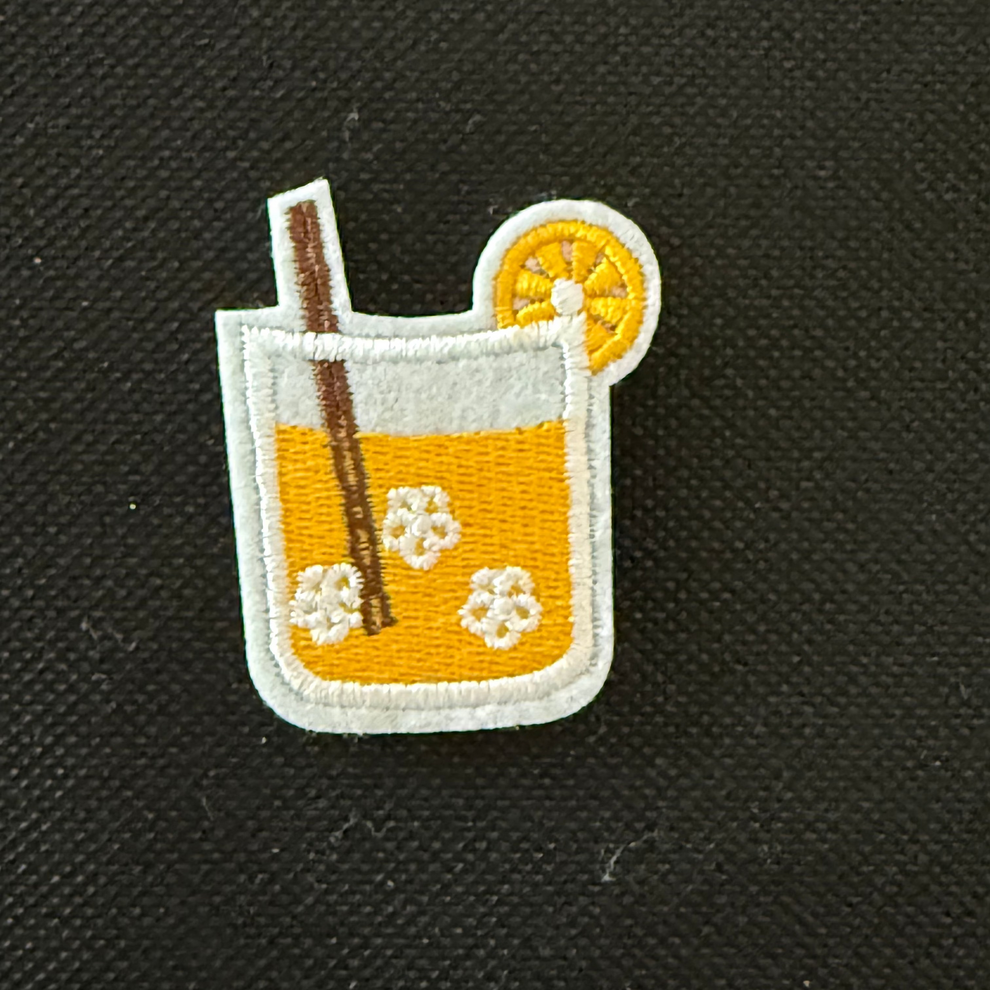 Embroidered patch of a cocktail with an orange slice and straw on a black background