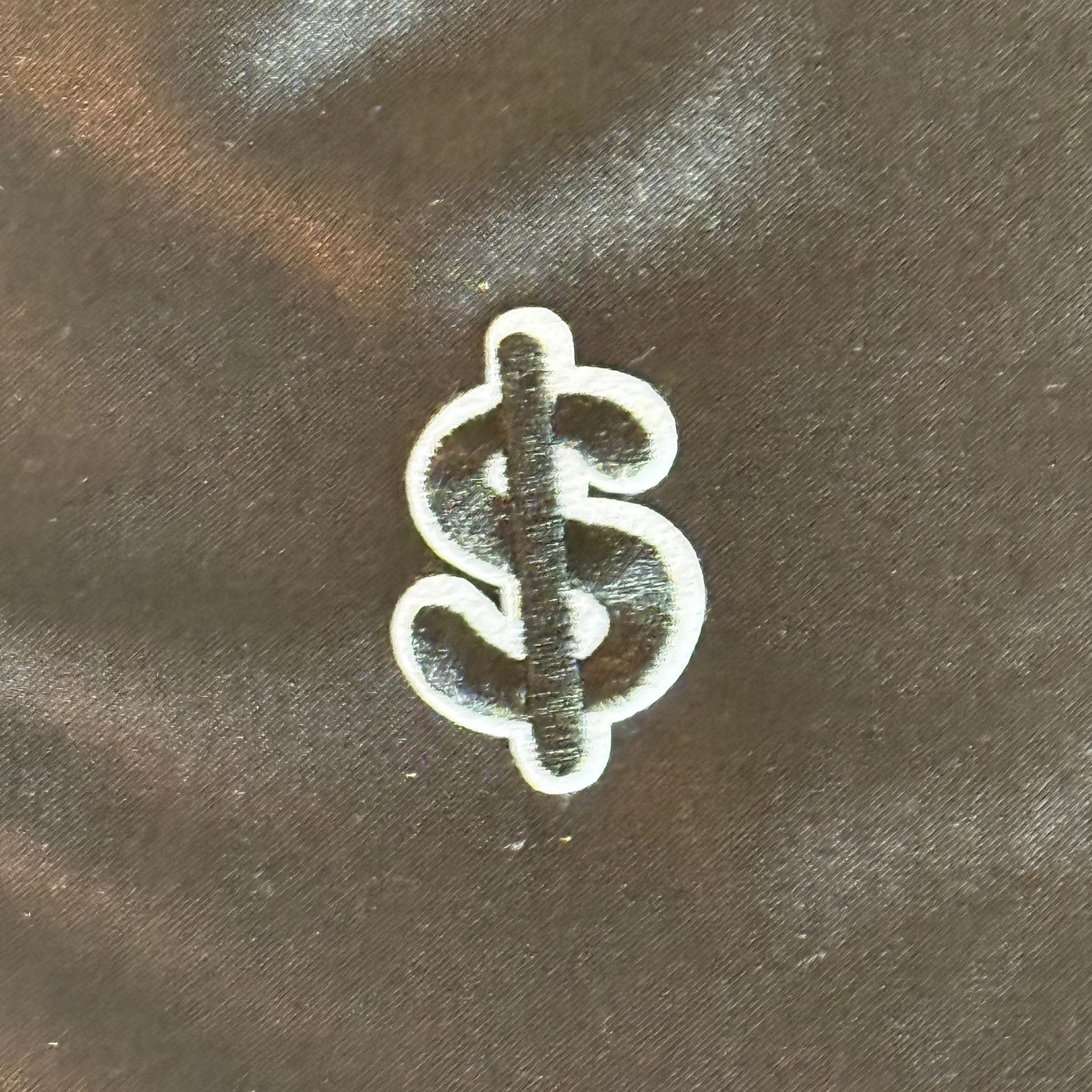 White and black dollar sign patch on a dark fabric background