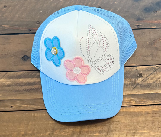 Blue and white cap with 2 flower design patches and a rhinestone butterfly wing. pic on a wooden surface