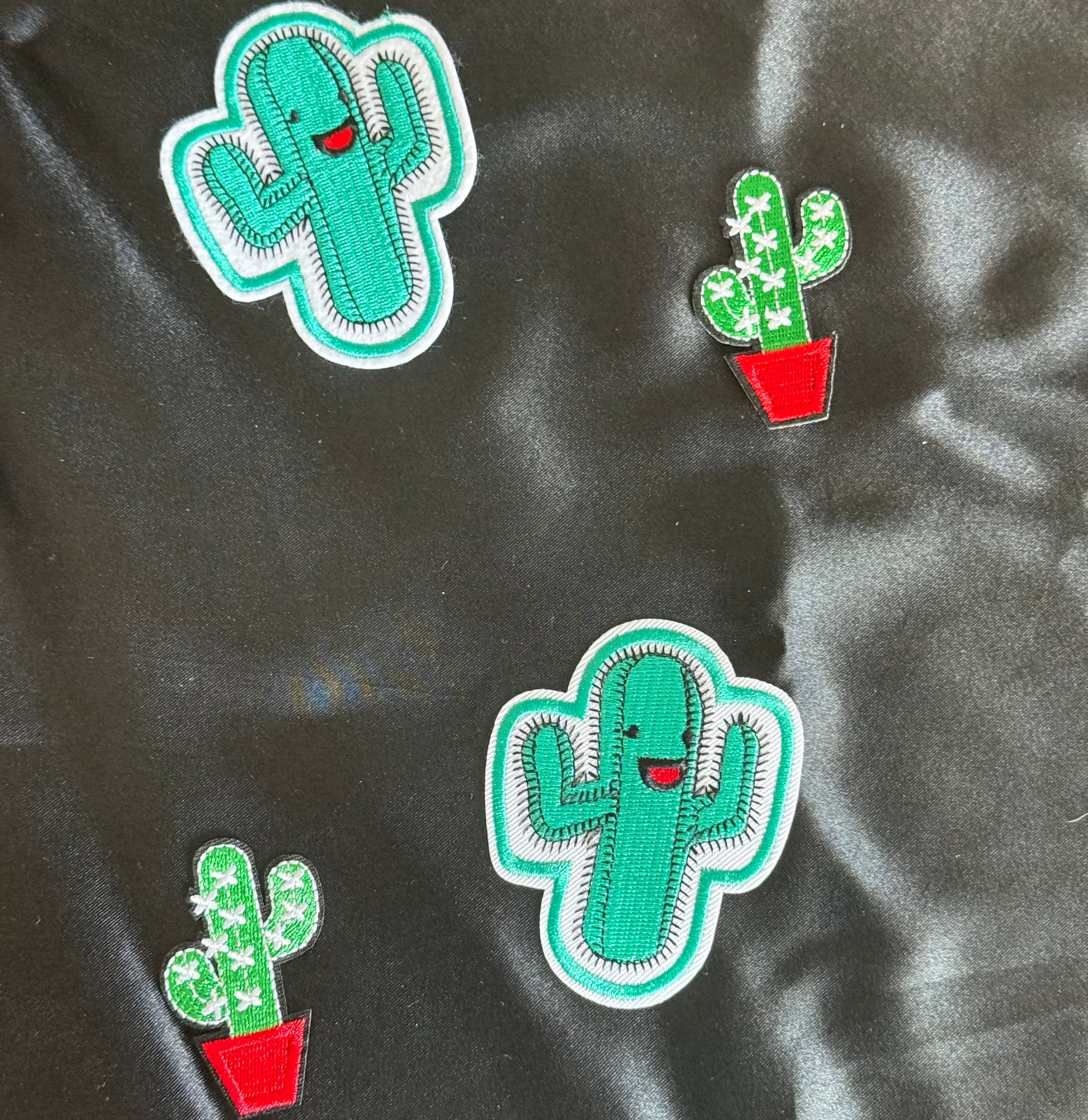 Four cactus-shaped patches on a black satin background