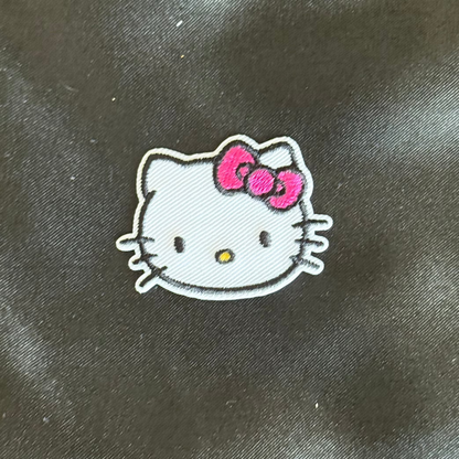Small cartoon character patch with a pink bow on a dark fabric background