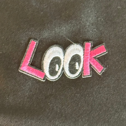 Embroidered patch with the word 'LOOK' placed on a dark fabric background