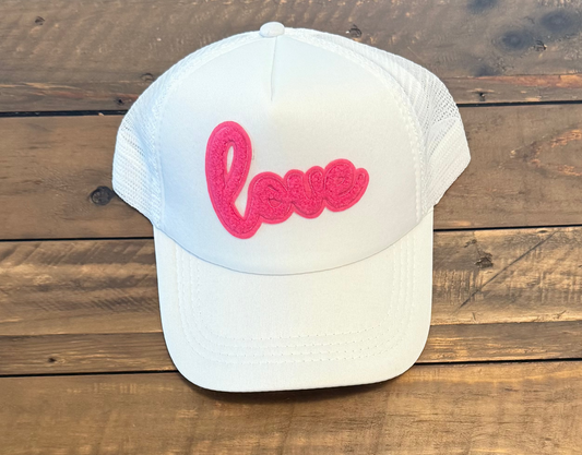 white on white hat with a pink cursive "love" patch on the front. wooden background