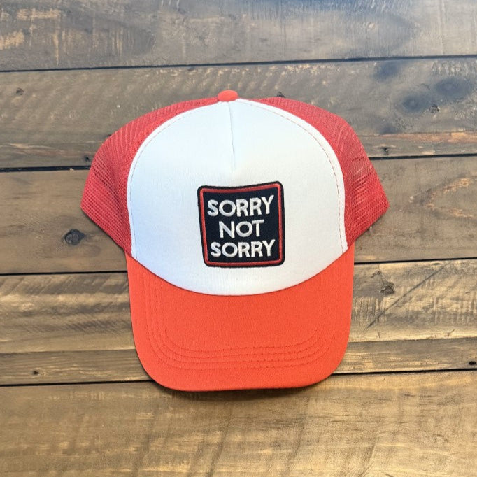 Red and white cap with a patch that says "Sorry Not Sorry" placed on a wooden background