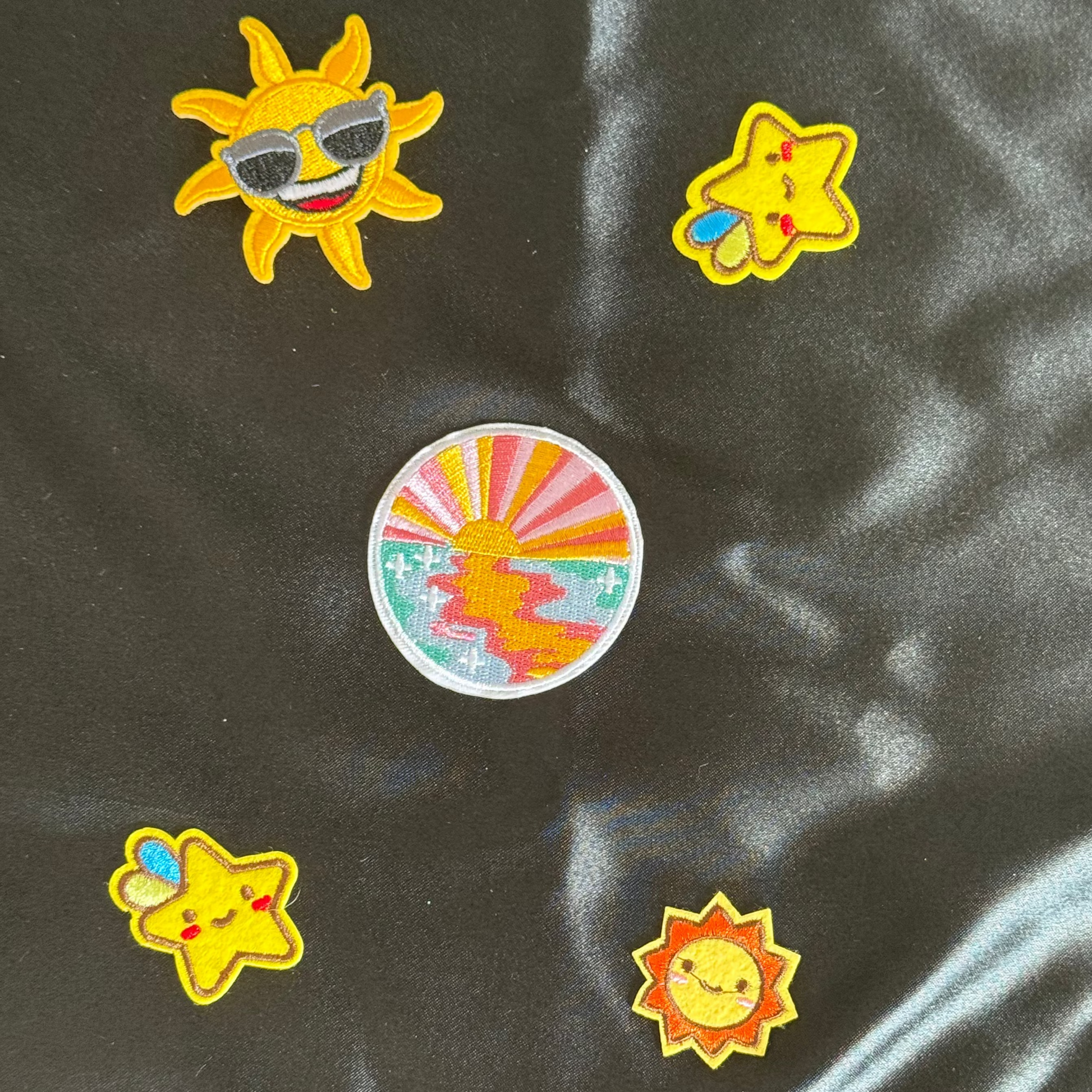 Colorful sun and star shaped patches on a black satin background