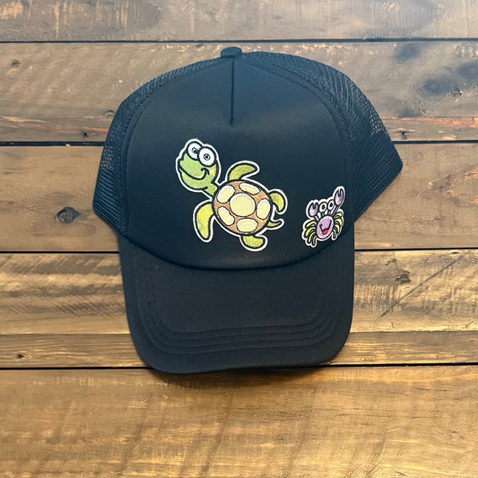 Black cap with a turtle design patch and a crab design patch on a wooden surface